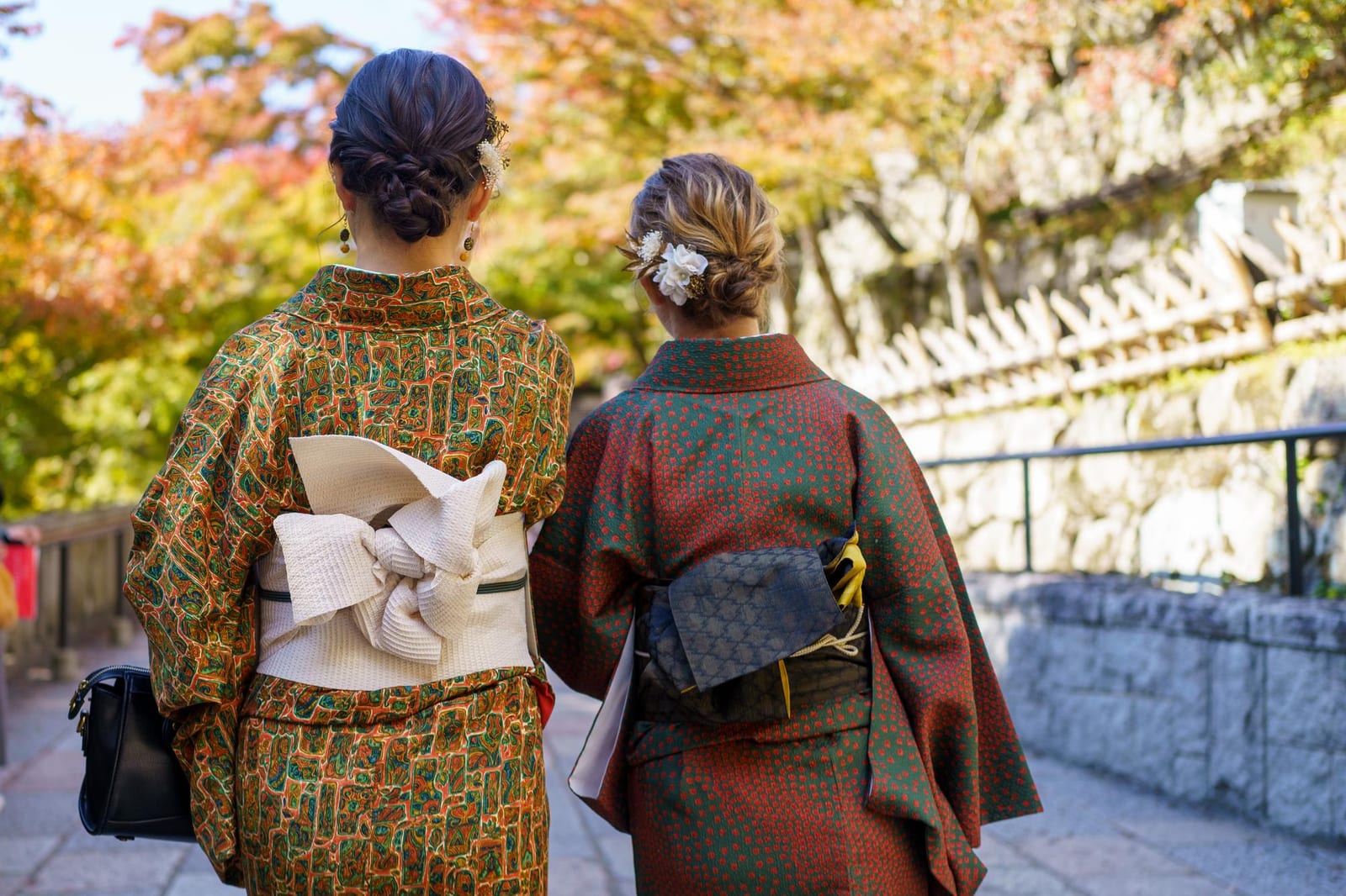 紅葉の参道を着物姿で歩く二人の女性。